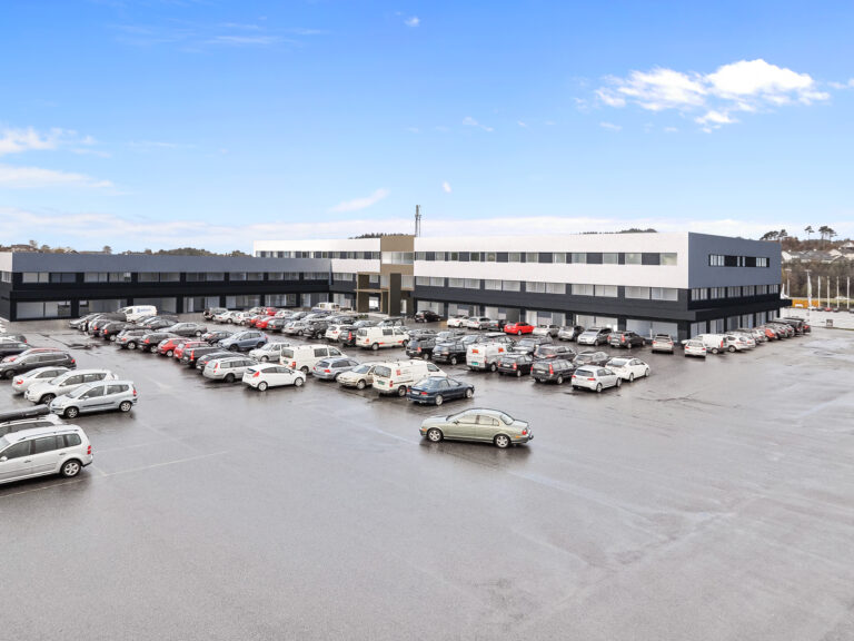 et stort kontorbygg med biler parkert på parkeringsplassen.